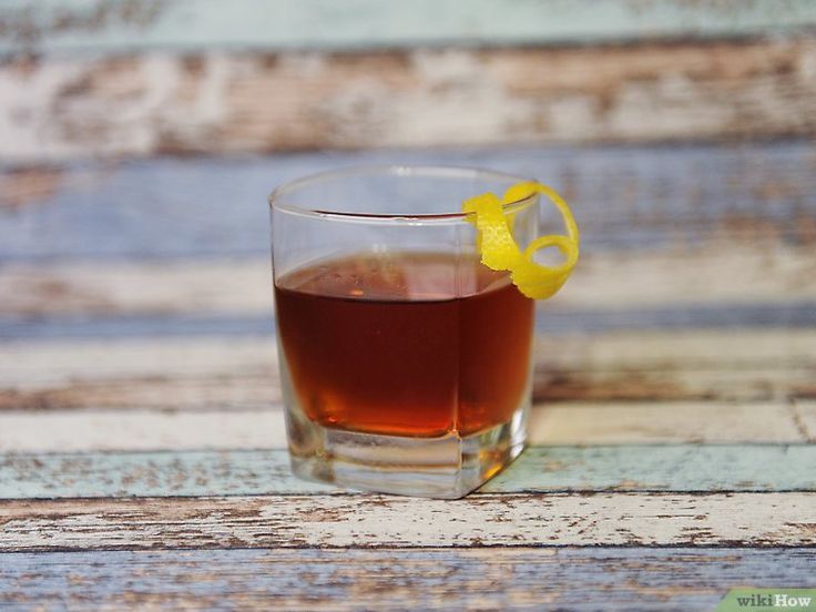 a glass filled with liquid sitting on top of a wooden table next to a lemon slice