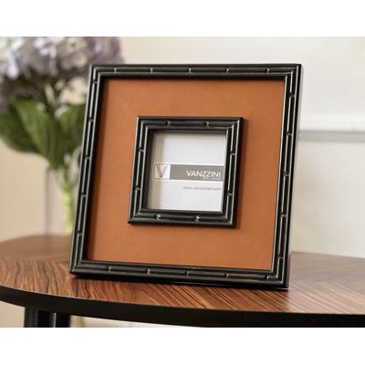 a wooden table with a black frame on top of it and flowers in the background