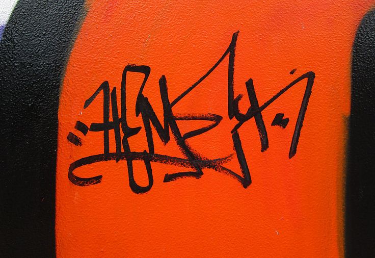 graffiti written on the side of a wall with orange and black paint in different languages