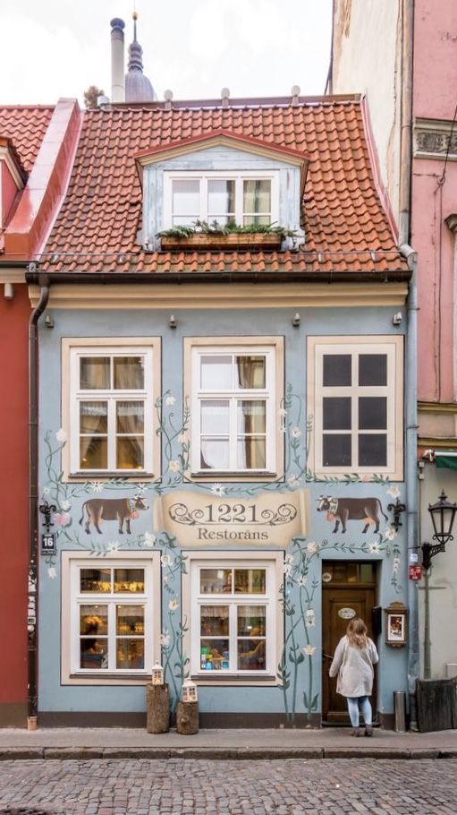 a woman is standing in front of a store on the side of a building with windows