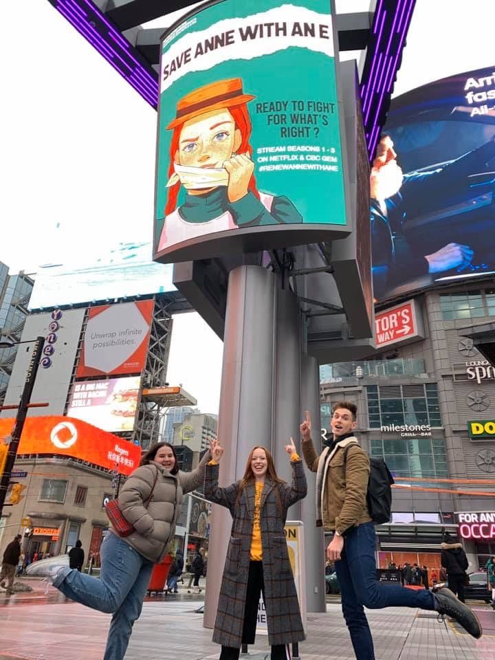 three people standing next to a street sign with an advertisement on it's side