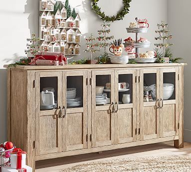 a wooden cabinet with christmas decorations and dishes on it's top, sitting in front of a white wall