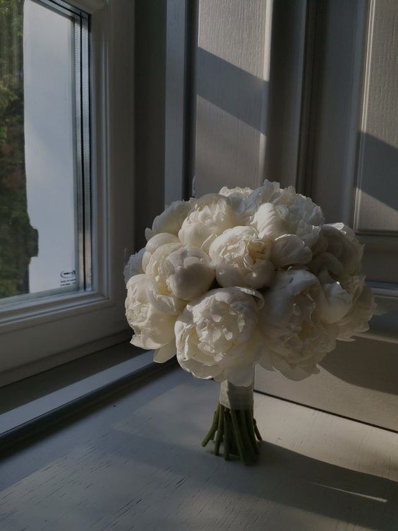 a bouquet of white peonies sitting on a window sill next to a window