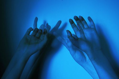 two hands reaching up into the air with their fingers in front of them, against a blue background