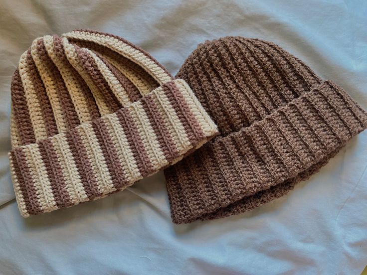 two crocheted hats laying on top of a bed