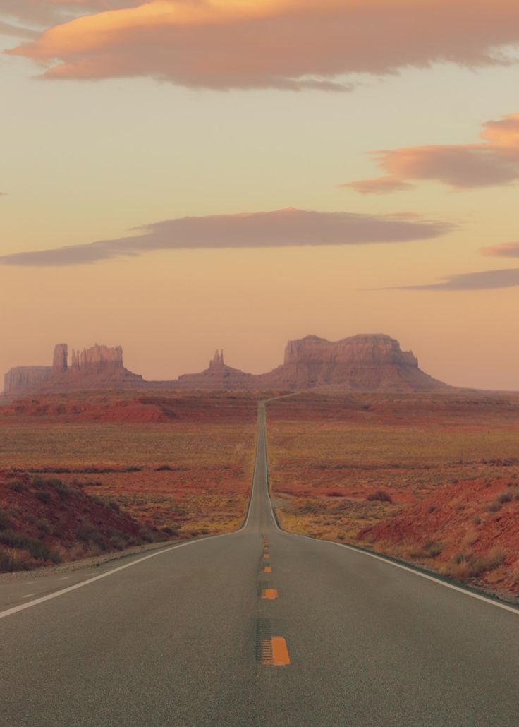 an empty road in the middle of nowhere with mountains in the background