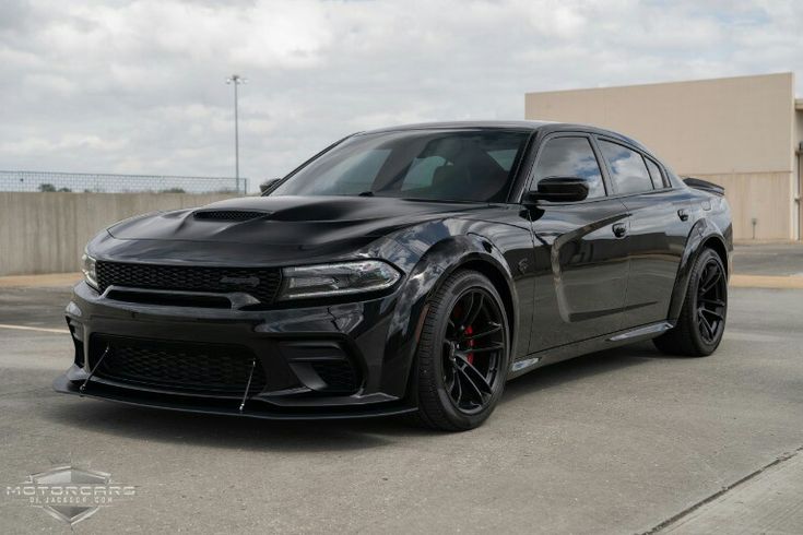 a black dodge charger is parked in a parking lot next to a building on a cloudy day