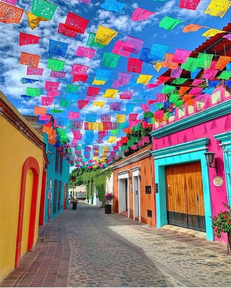 there are many colorful flags hanging in the air on this street that's lined with buildings