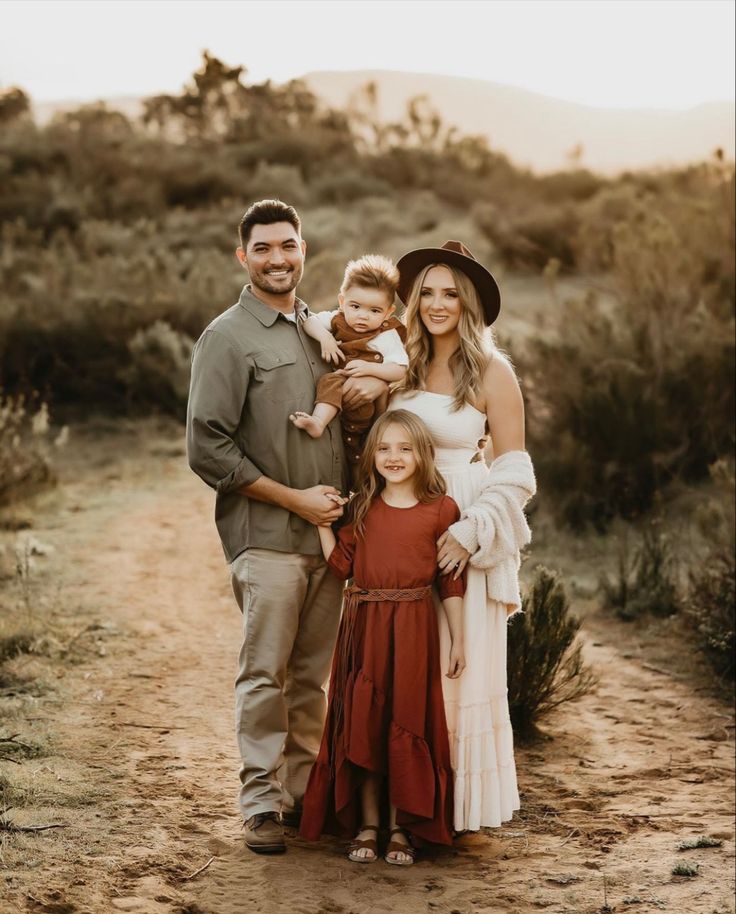 a family posing for a photo on a dirt road in front of bushes and trees