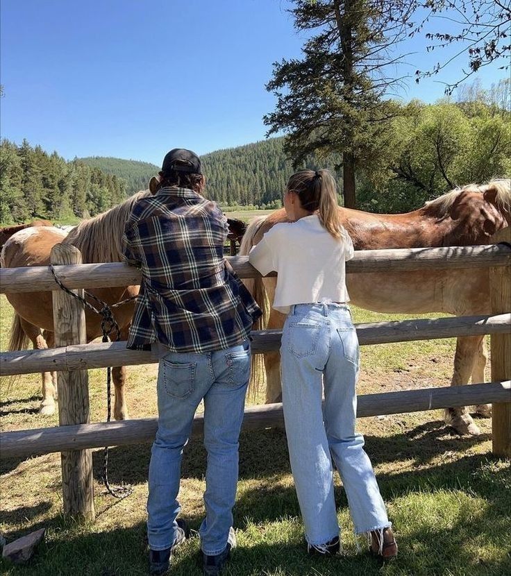 two people standing next to a fence with horses