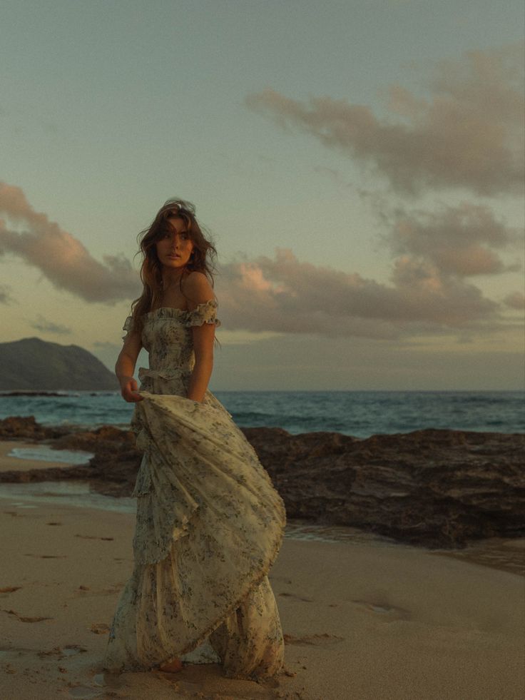 a woman standing on top of a sandy beach next to the ocean wearing a dress