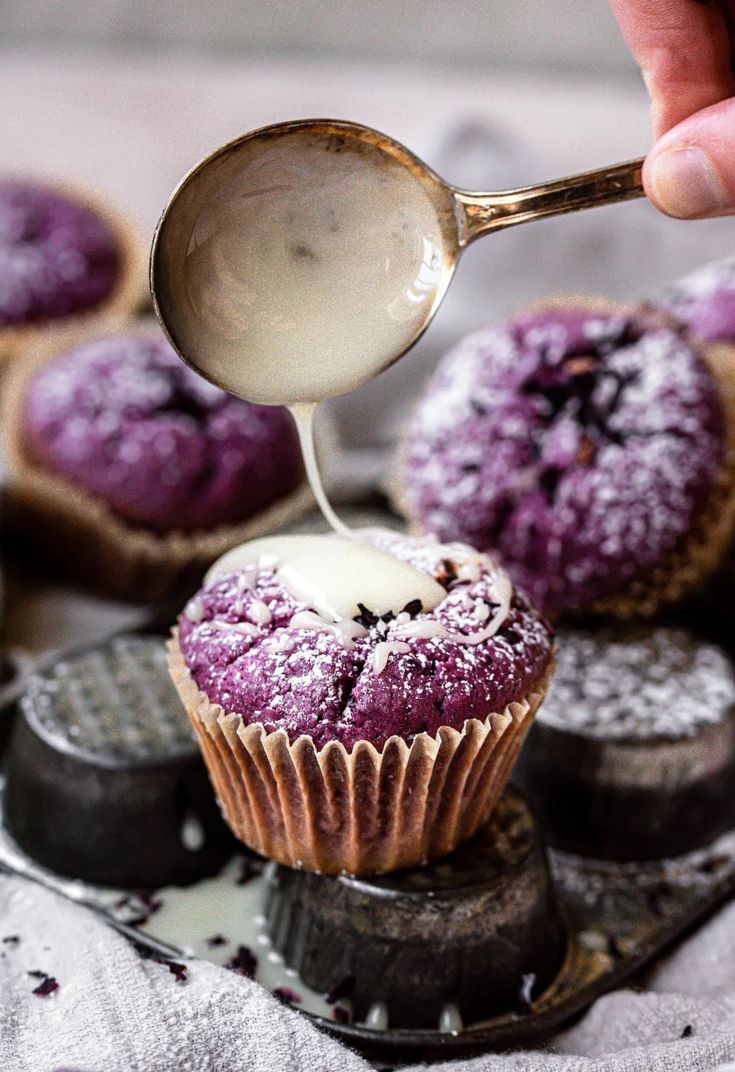 a spoon is pouring sugar on some cupcakes