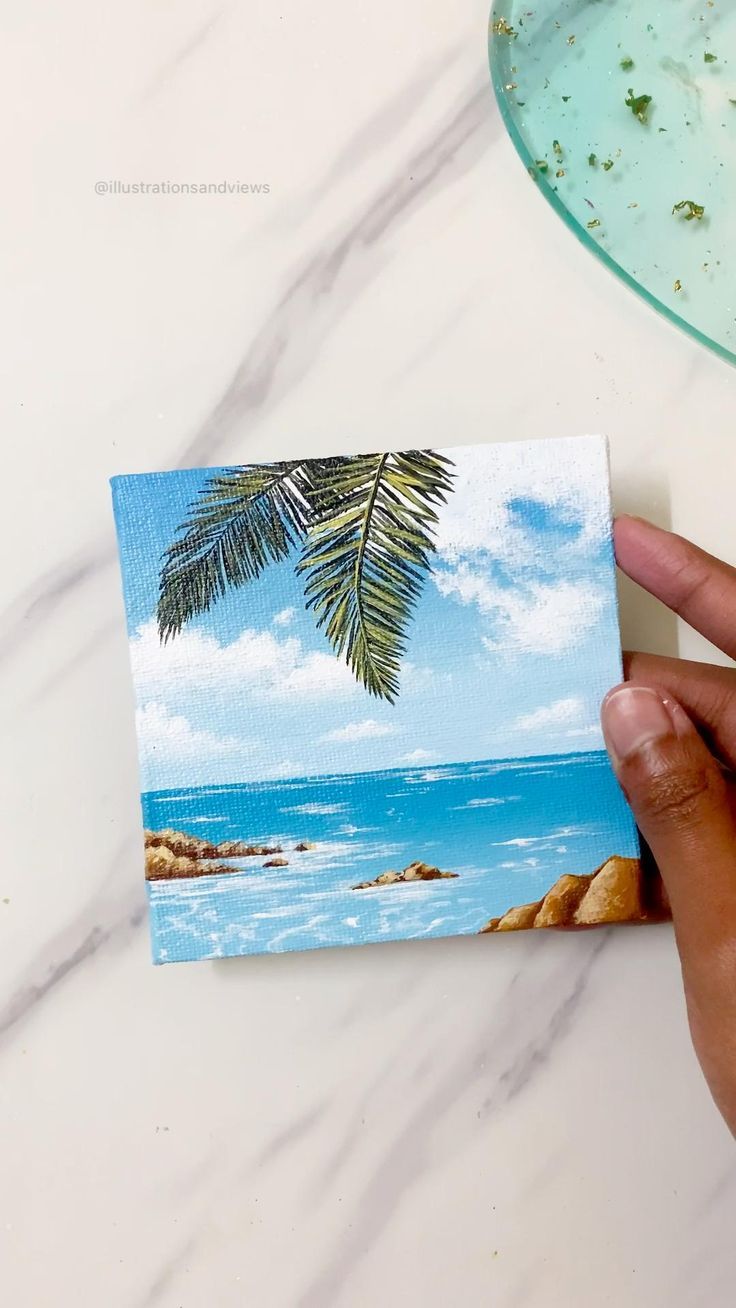 a person holding up a piece of paper with a palm tree on the beach in the background