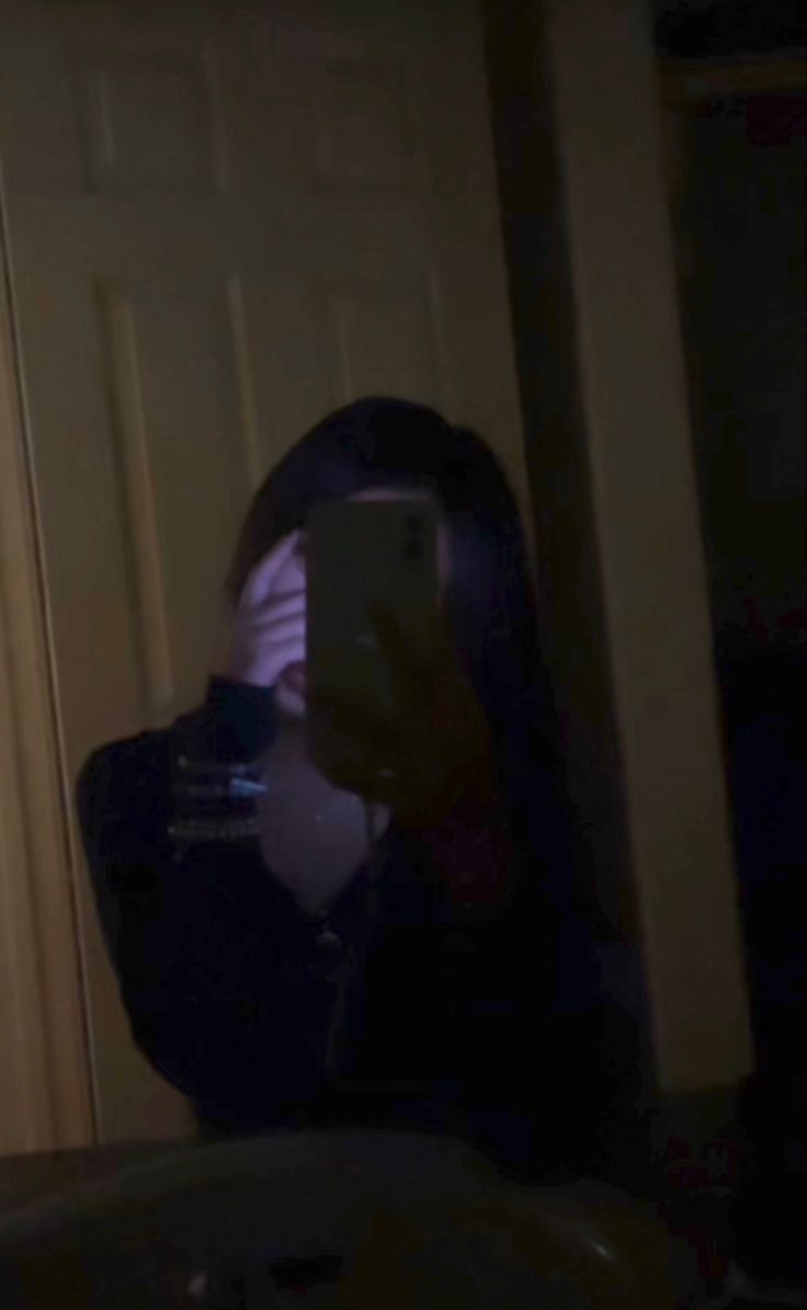 a woman taking a selfie in the mirror with her cell phone at night time