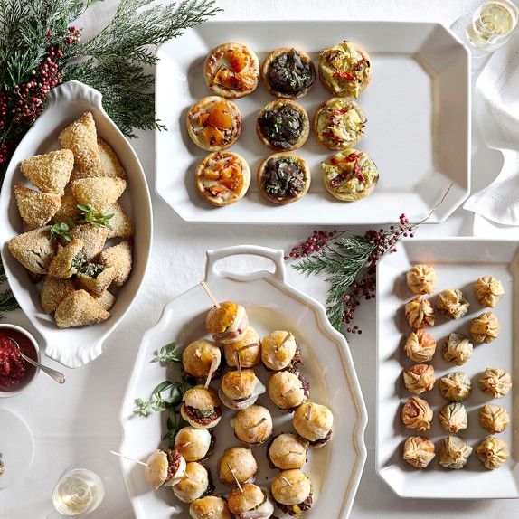 an assortment of appetizers on serving trays next to wine glasses and christmas decorations