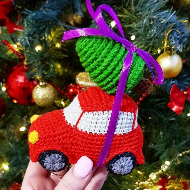 a hand holding a small red car ornament in front of a christmas tree