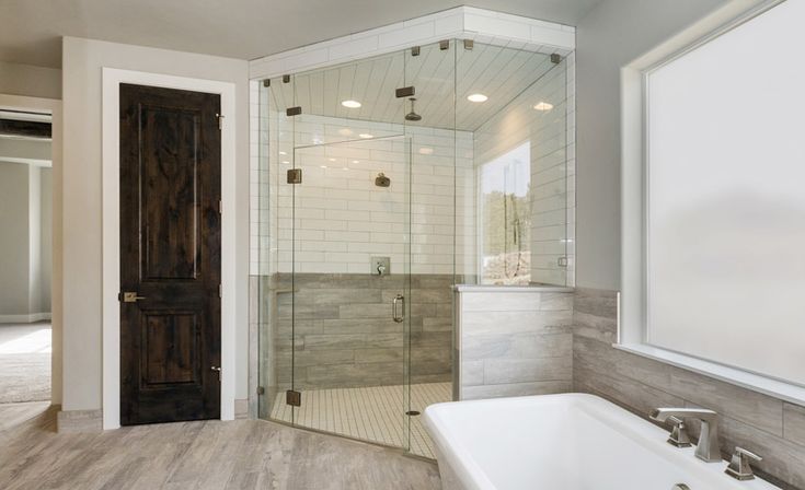 a bathroom with a walk in shower next to a white bath tub and wooden door