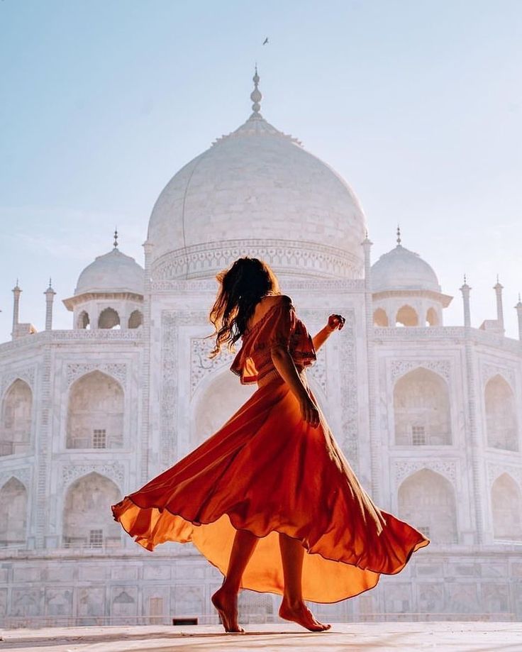 a woman in an orange dress is walking near the tajwa mosque, india