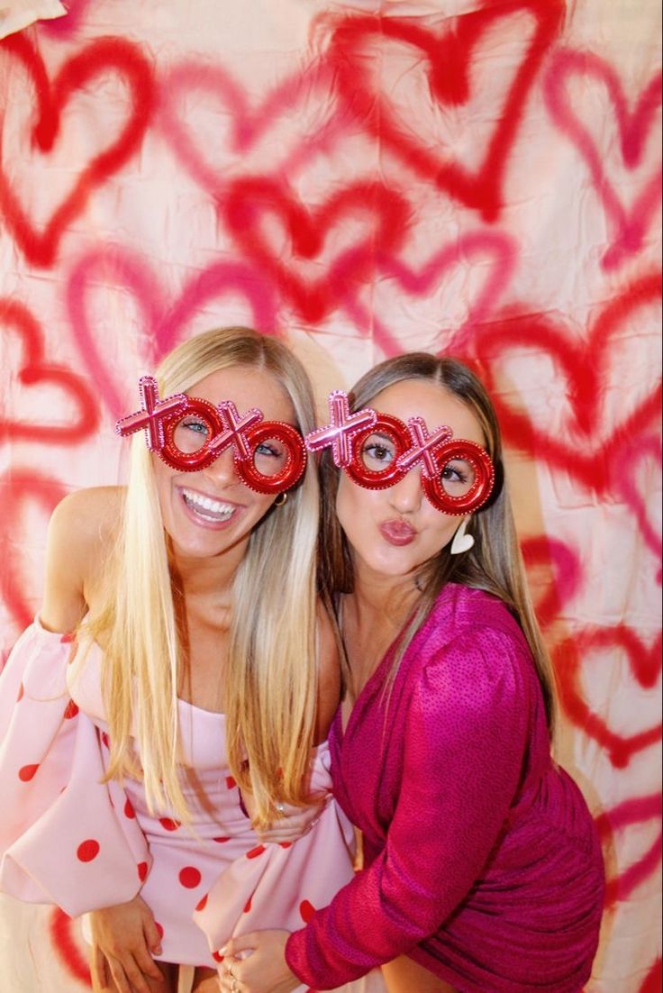 two beautiful young women standing next to each other in front of a wall with hearts painted on it