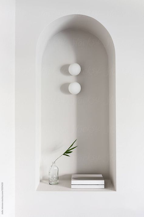 a white wall with three lights and a vase on the shelf next to it by an arch