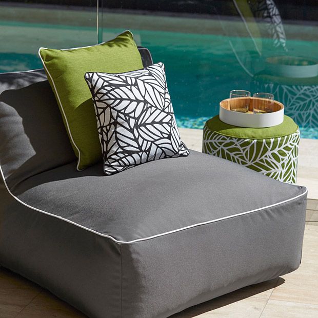 an outdoor lounge chair next to a swimming pool with pillows on the seat and side table