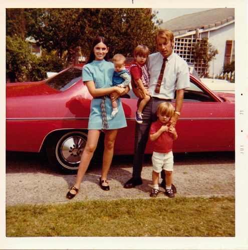 a family poses in front of a red car