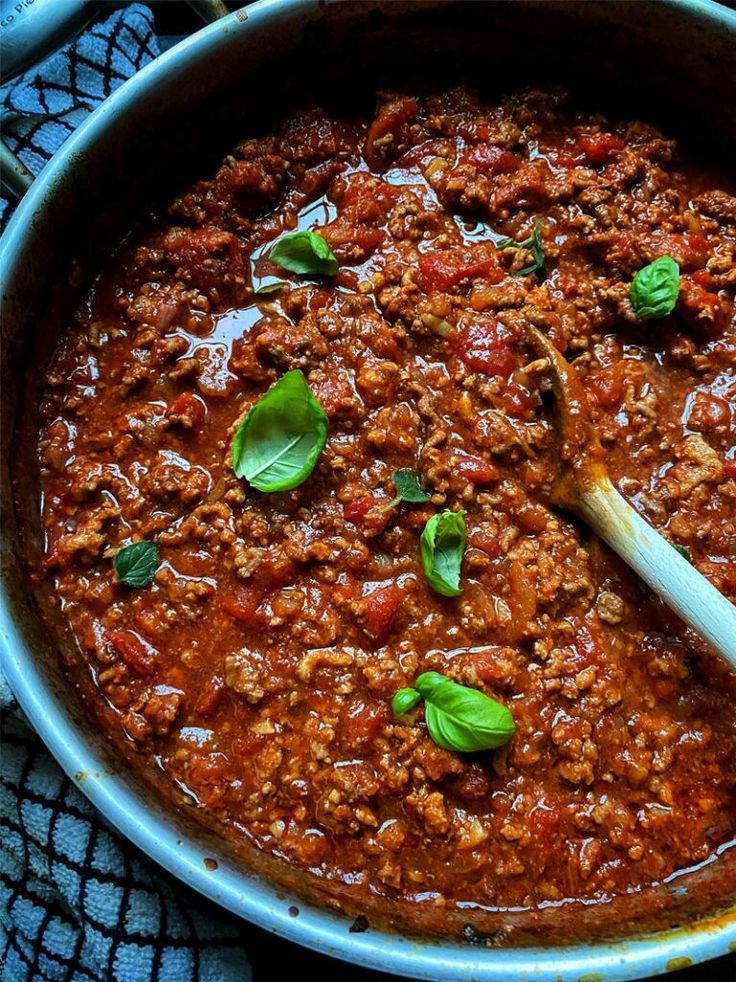 a large pot filled with meat and sauce on top of a table next to a wooden spoon