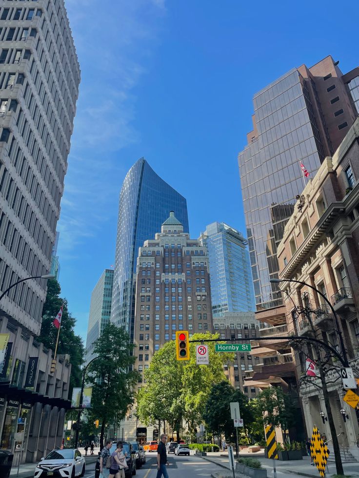 people are walking down the street in front of tall buildings and skyscrapers on a sunny day