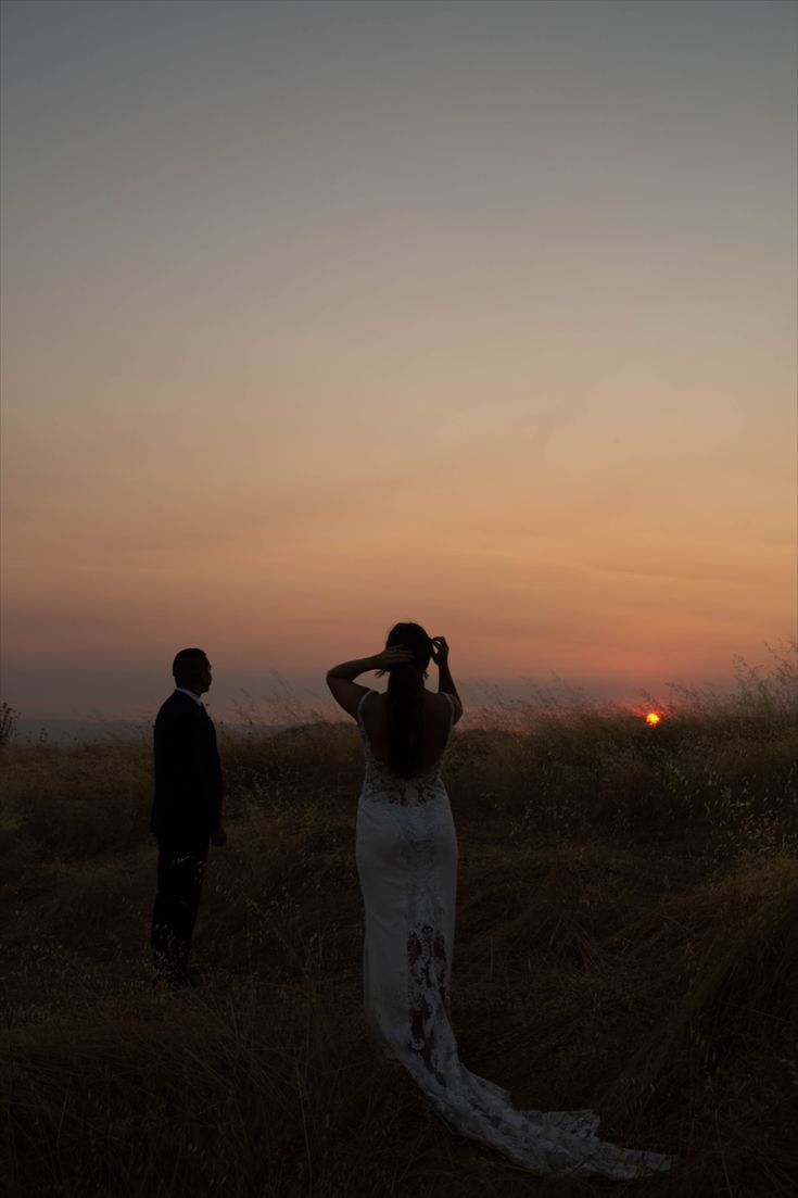 a woman in a wedding dress standing next to a man on top of a hill