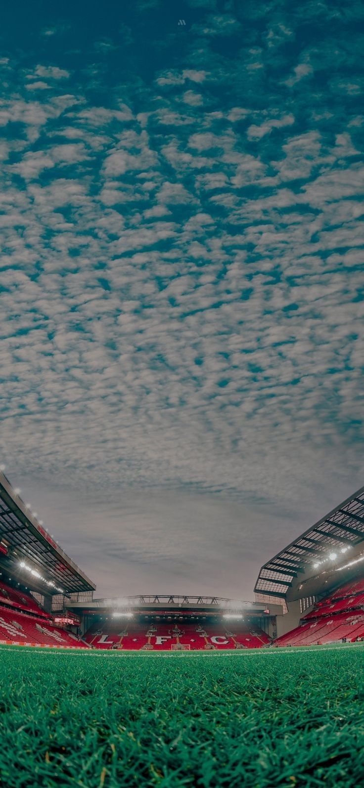 an empty soccer stadium with red seats and green grass under a cloudy blue sky at night