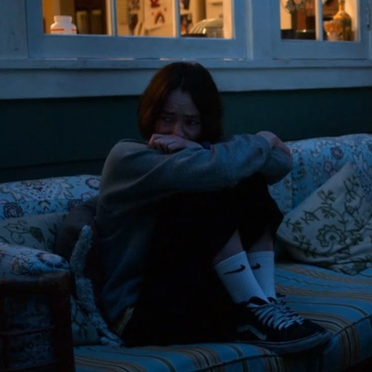 a woman sitting on top of a couch in front of a window with her arms crossed