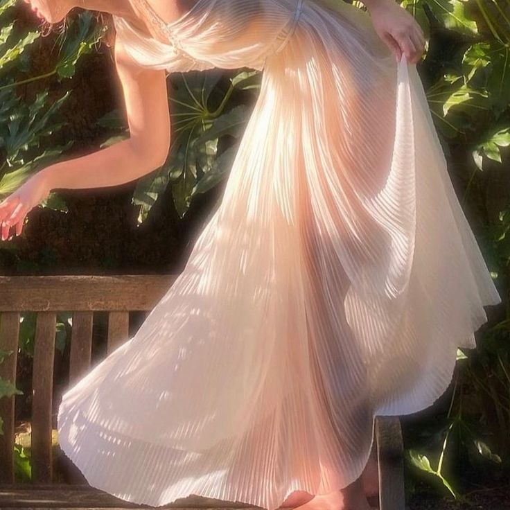 a woman in a long dress leaning on a bench