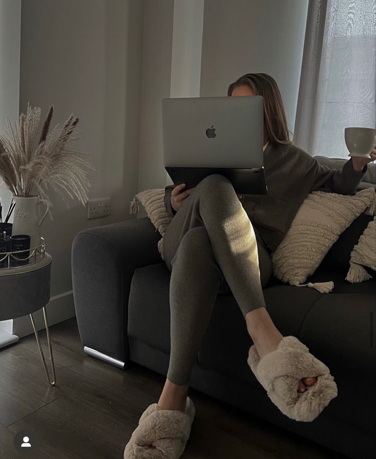 a woman sitting on a couch with her legs crossed and holding a laptop computer in front of her face