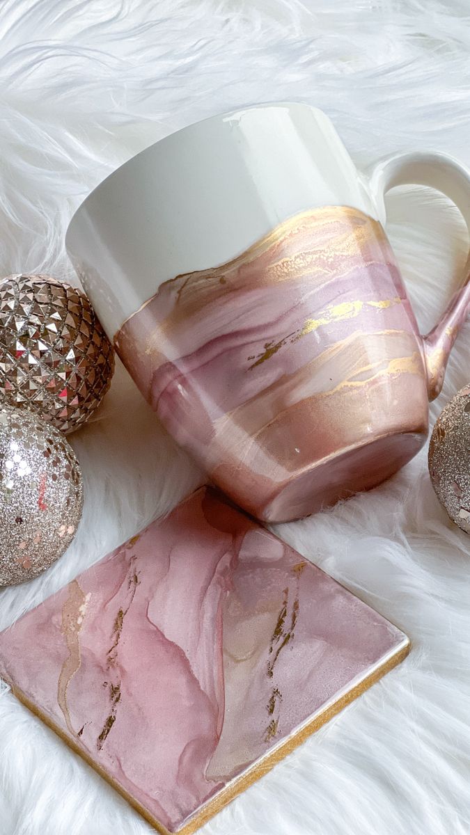 a pink marbled coffee mug sitting on top of a white fur covered floor next to ornaments