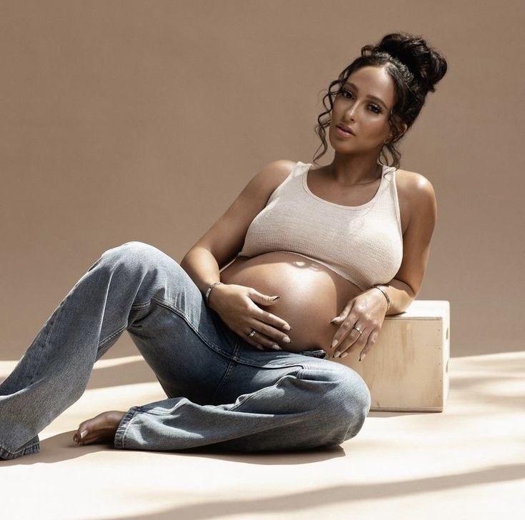 a pregnant woman sitting on the ground with her belly up and hands in her pockets