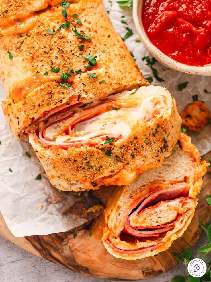 a sandwich cut in half on top of a wooden cutting board next to a bowl of tomato sauce