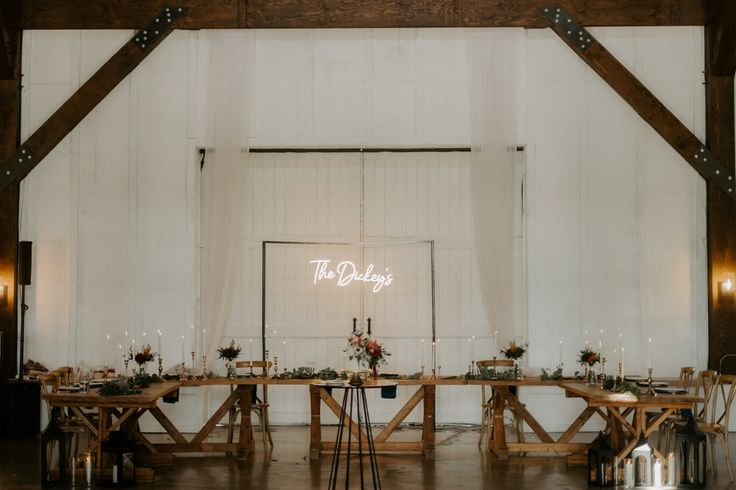 a long table set up with candles and flowers in front of a large white wall