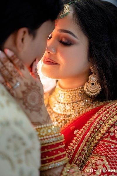 a woman in a red and gold outfit is kissing another woman's face with her hands on her chest