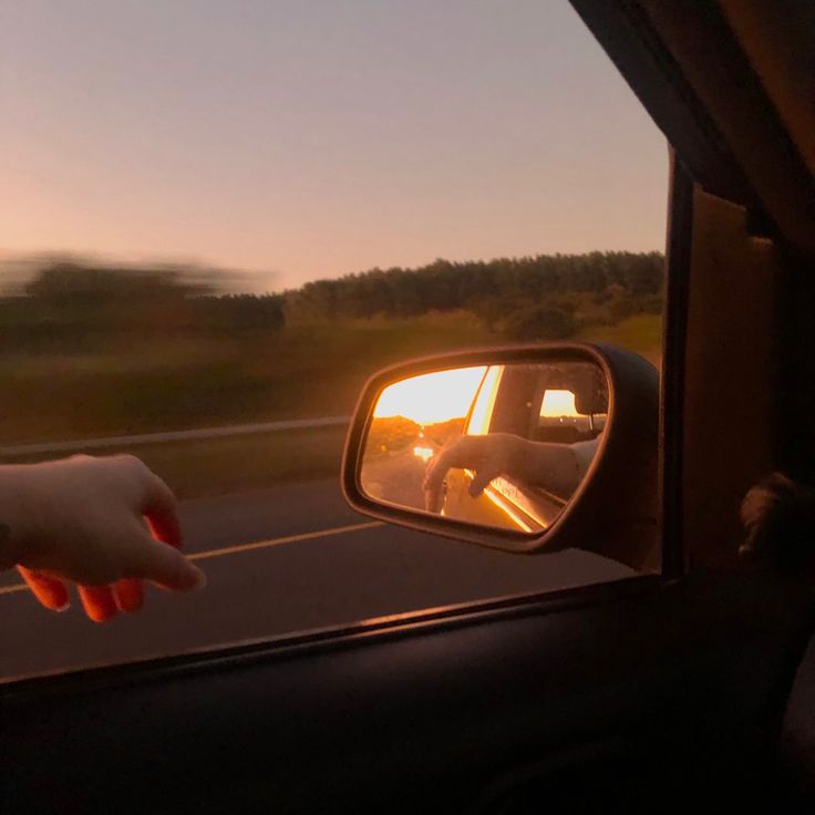 someone's reflection in the side view mirror of a car as it drives by