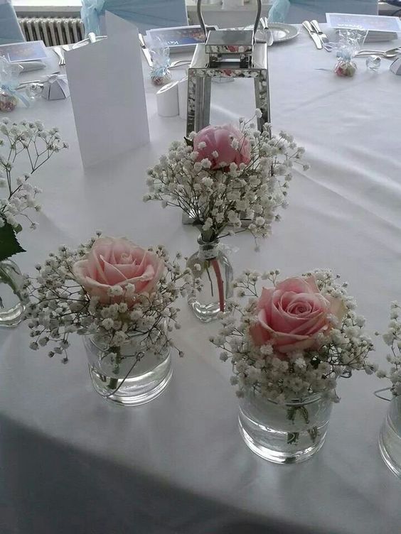 four vases filled with pink roses and baby's breath flowers on a table