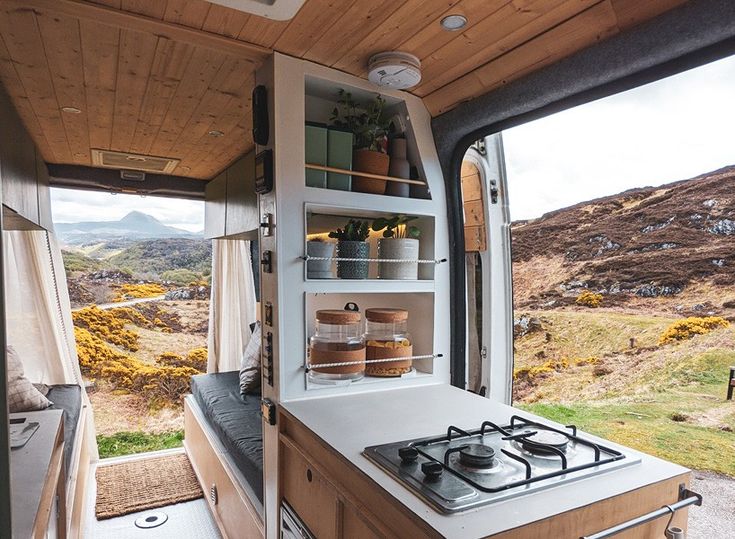 the interior of a camper with open doors and shelves on the side, looking out at mountains