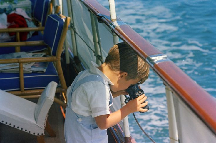 a young boy holding a camera on top of a boat