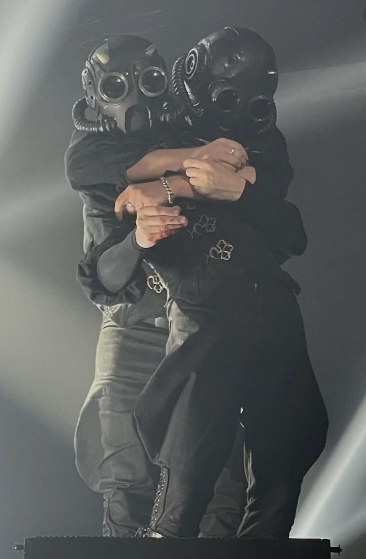 two people in gas masks hugging each other on stage with their arms around one another