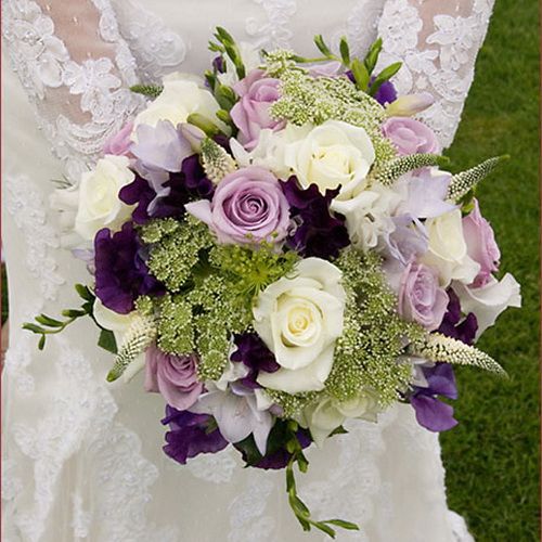 a bridal bouquet with purple and white flowers in the bride's wedding dress