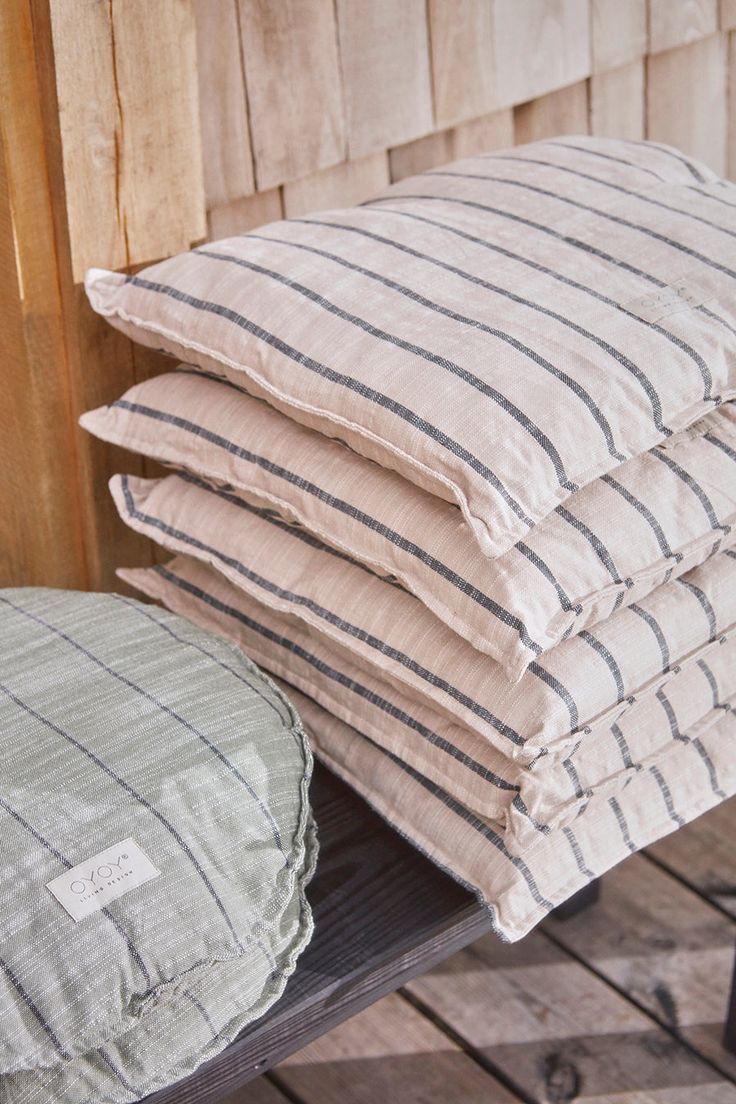 four pillows stacked on top of each other next to a wooden bench in front of a wall