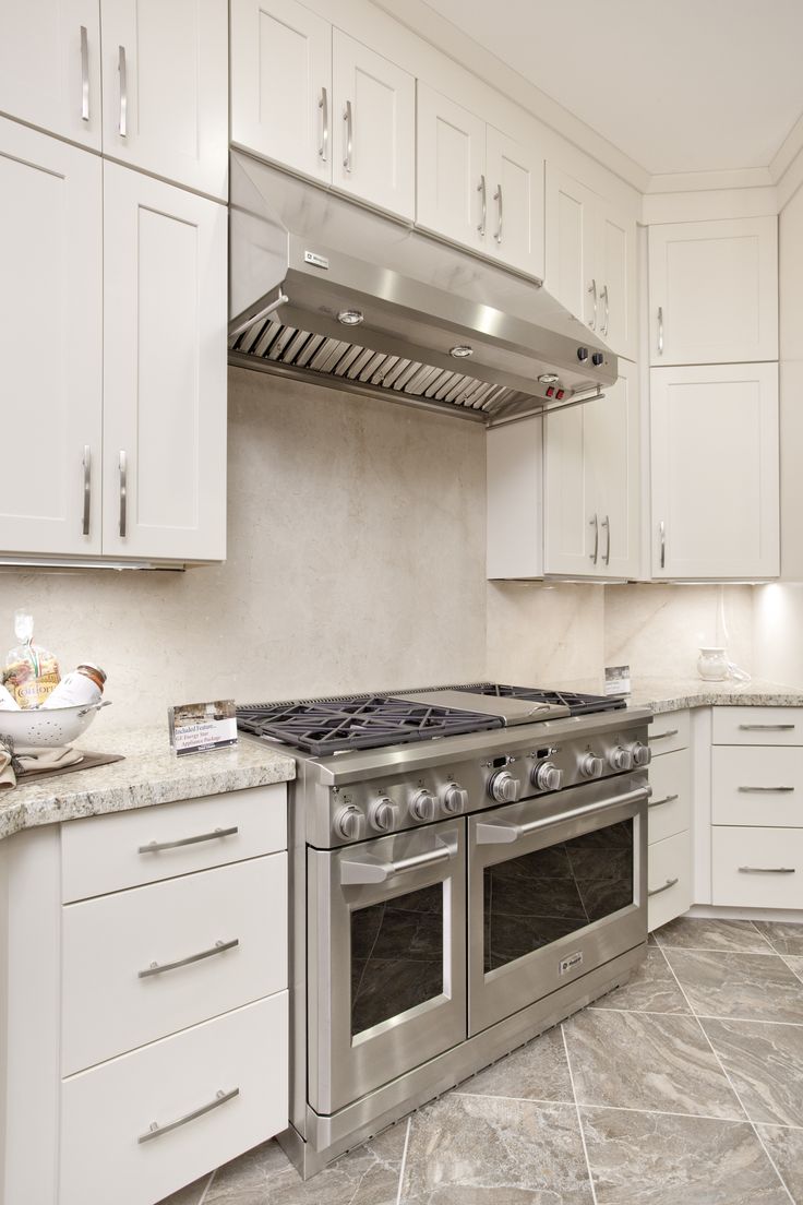 a kitchen with white cabinets and stainless steel stove top oven in the middle of it