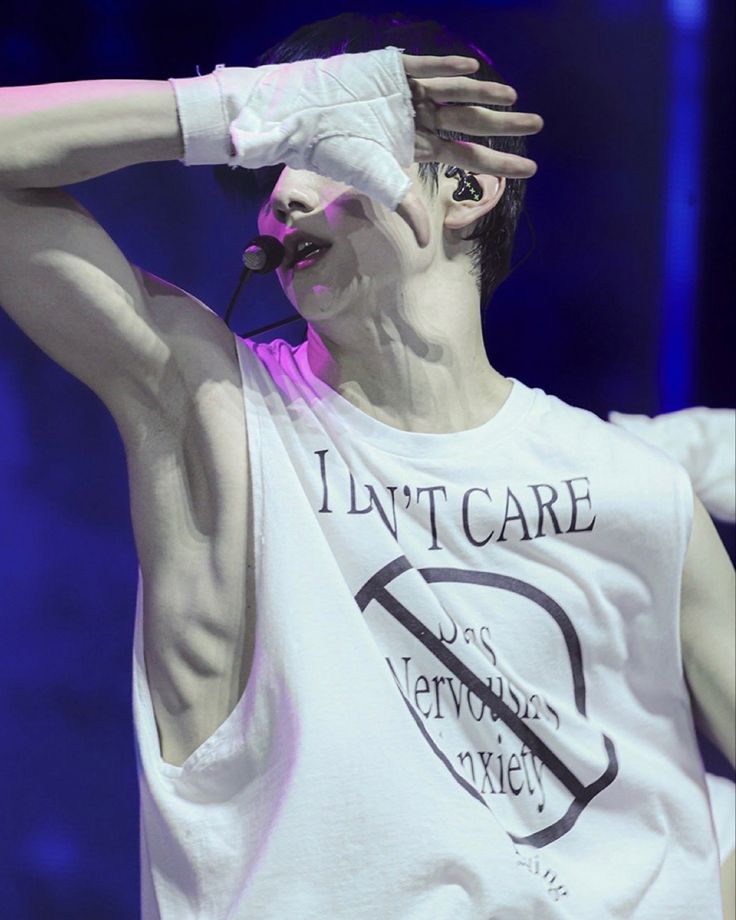 a male in a white tank top is holding his hands up to his head while standing on stage