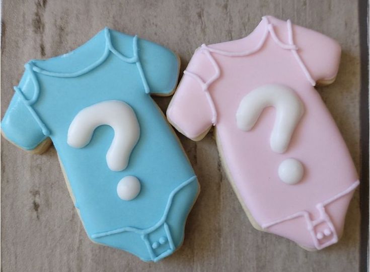 two decorated cookies in the shape of baby ones with question marks on them, one blue and one pink