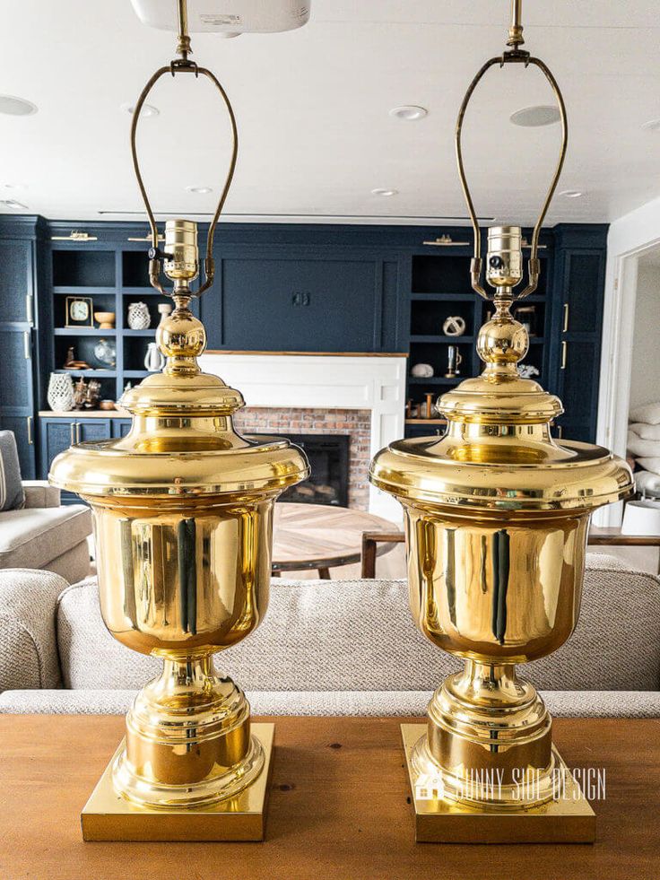 two brass lamps sitting on top of a wooden table