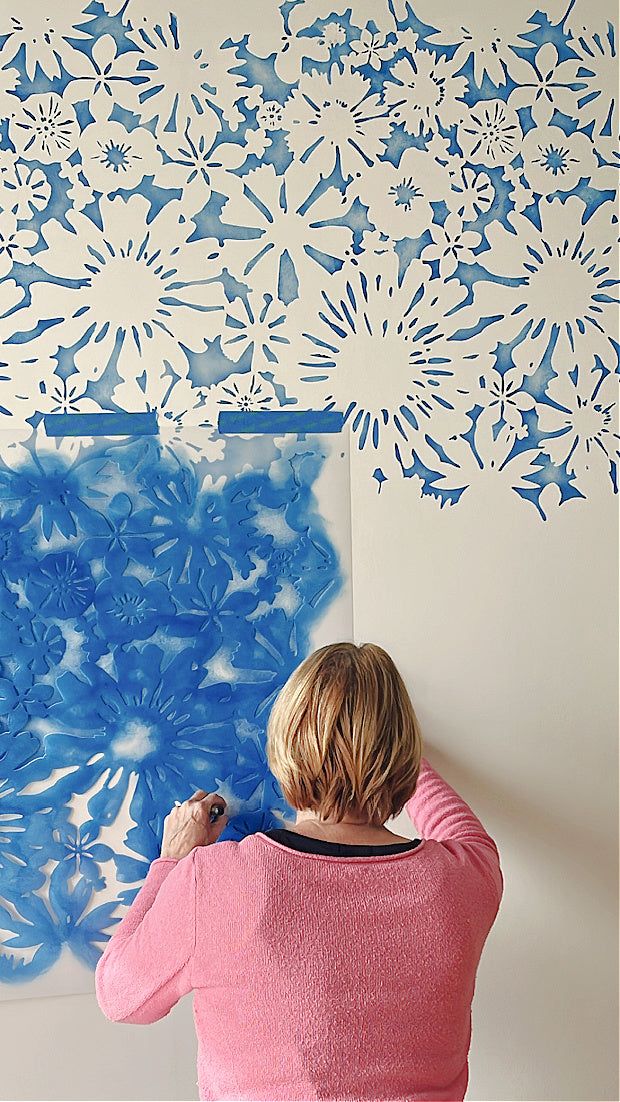 a woman is painting on the wall with blue stencils and white paper flowers